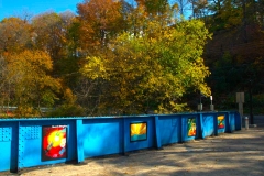 Four paintings adorn the blue bridge as autumn trees stand behind on the Karl Stirner Arts Trail in Easton, Pennsylvania.